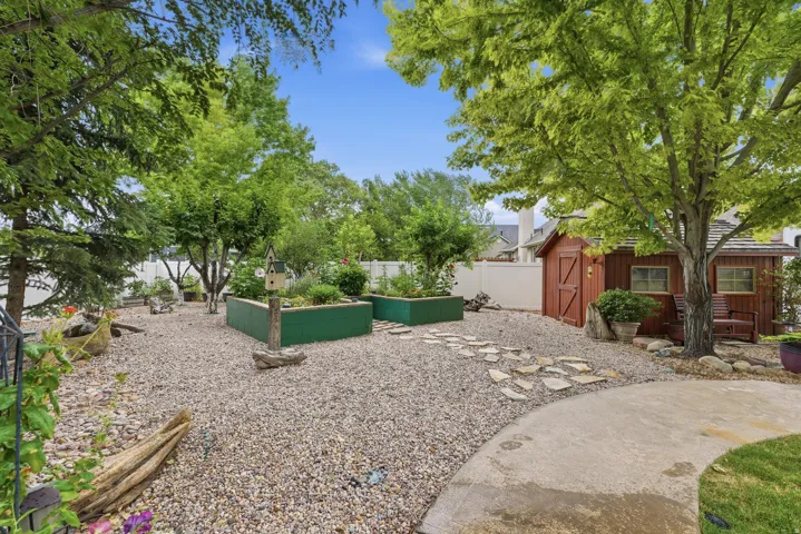 Gravel-covered backyard featuring multiple mature trees and a concrete patio