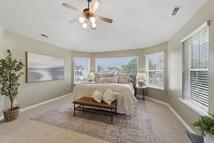 Spacious bedroom featuring a vaulted ceiling, ceiling fan with integrated lighting, multiple windows with blinds, and carpeted flooring