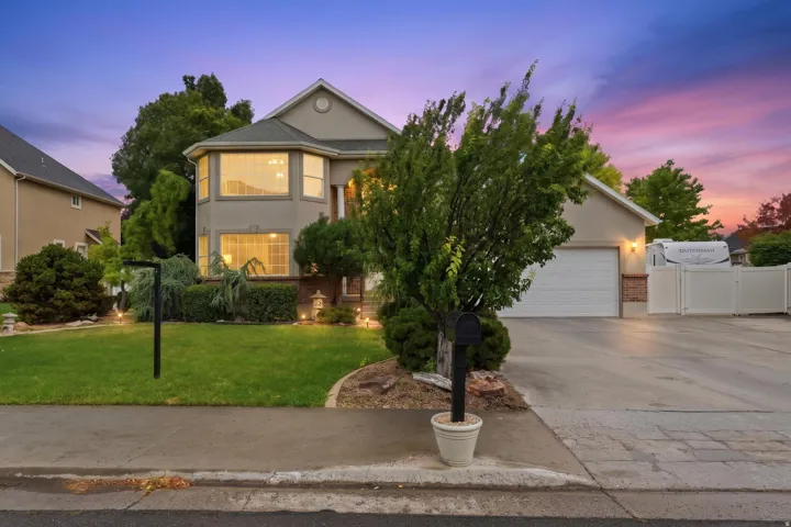 Stucco-sided residence featuring a two-car garage, mature landscaping, and a bay window