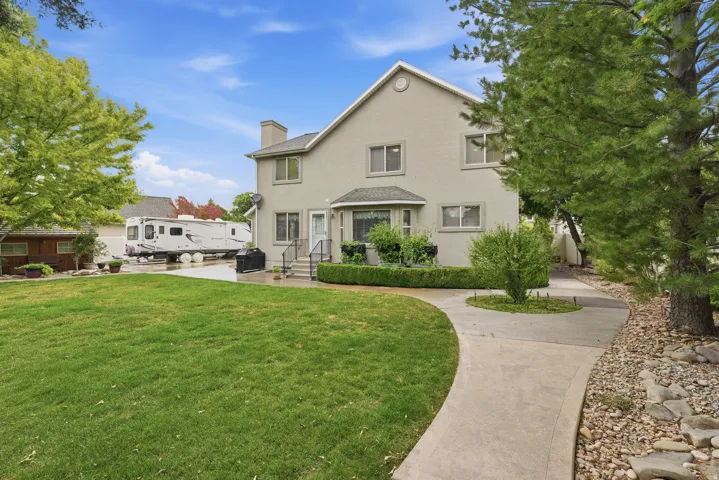 Expansive rear yard featuring a manicured lawn, concrete pathway, and mature trees