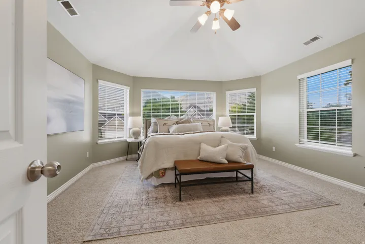 Spacious bedroom featuring light neutral wall tones, plush carpet flooring, and a ceiling fan with integrated lighting