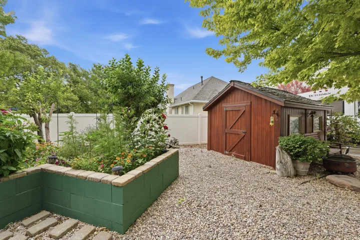 Backyard featuring a wooden storage shed with a shingle roof, a gravel patio area, a raised garden bed with a stone block border, and a privacy fence