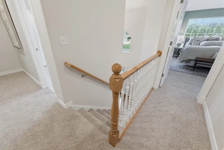 Carpeted hallway and staircase featuring light wood-finish railings, white balusters, and painted walls