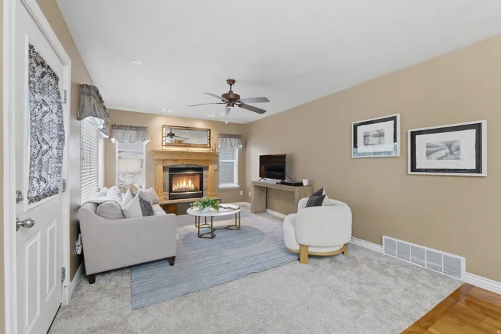 Living area featuring a stone-surround fireplace with a wood mantle, a ceiling fan, and carpet flooring