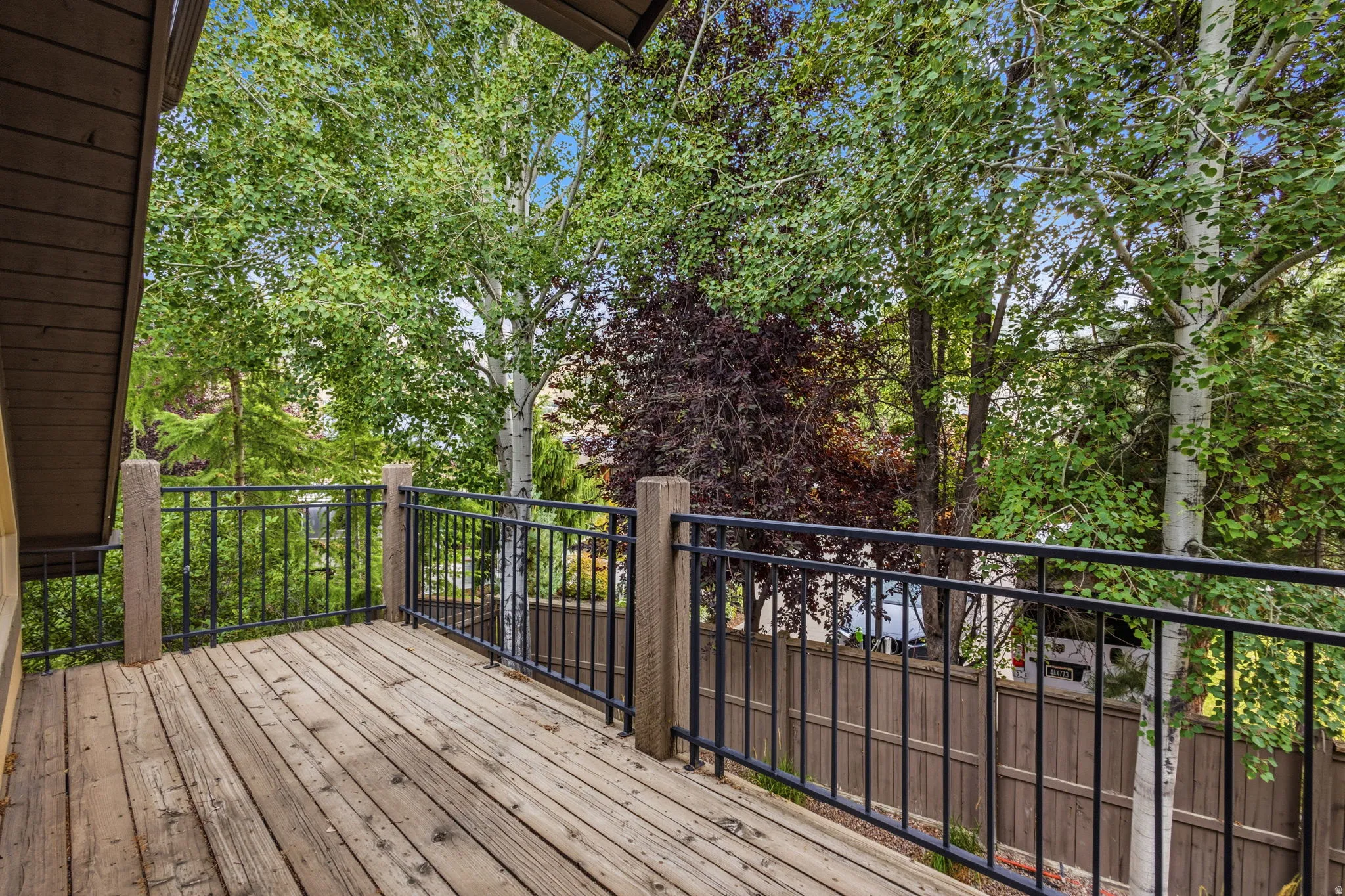 Wood-finish deck with black metal railings, surrounded by mature trees
