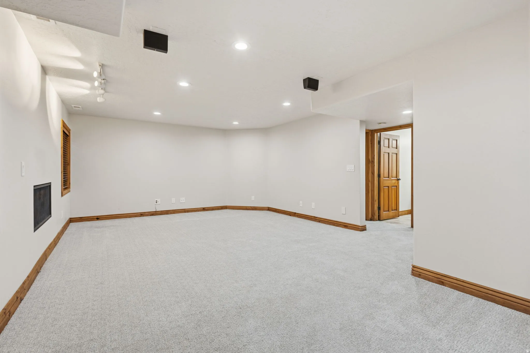 Expansive carpeted room featuring recessed lighting, a wood-trimmed window, a dark-toned wall register, and warm wood baseboards