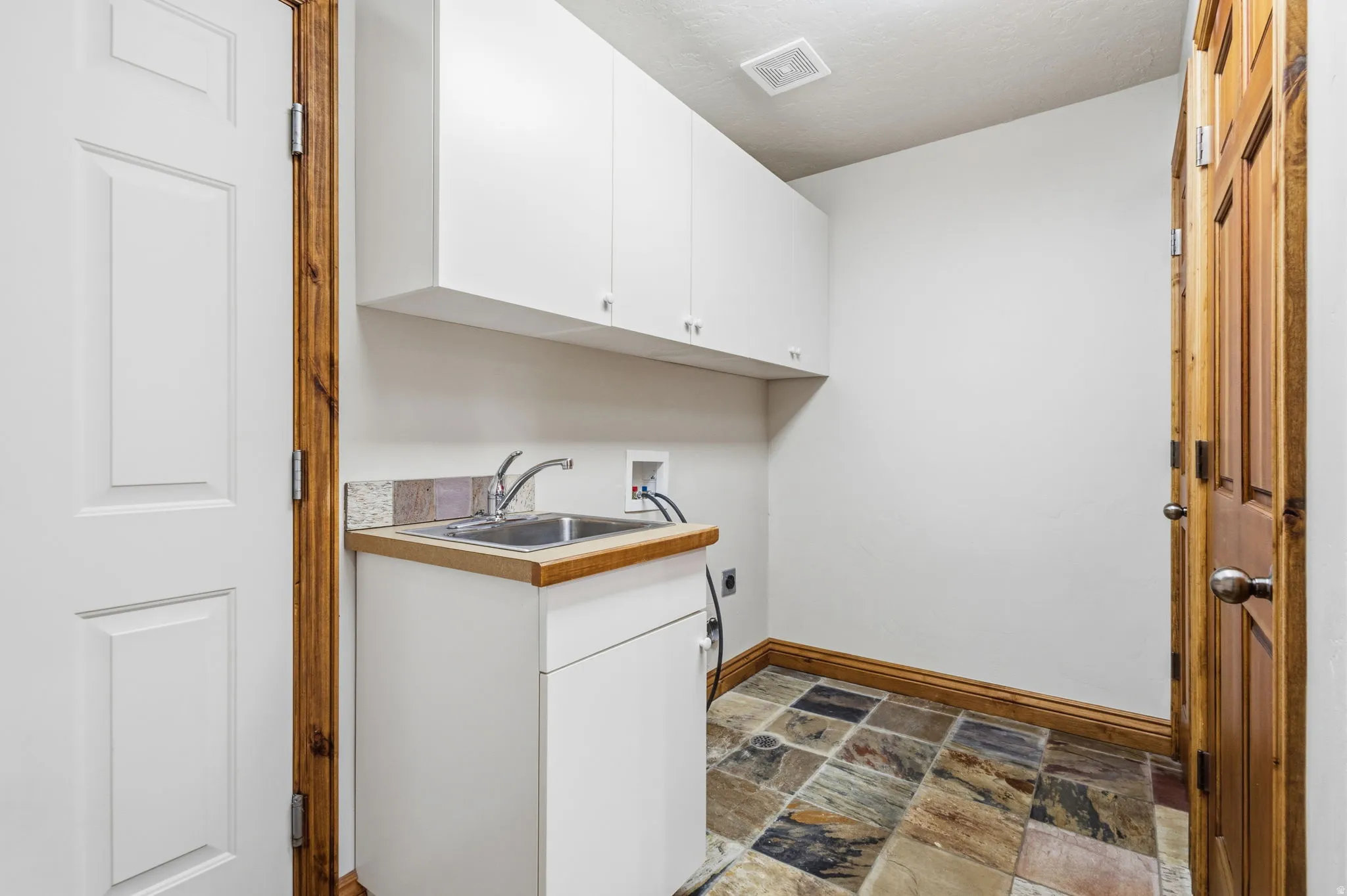 Utility area featuring white cabinetry with brushed nickel hardware, a stainless steel sink with a chrome faucet, and a wood-finish countertop