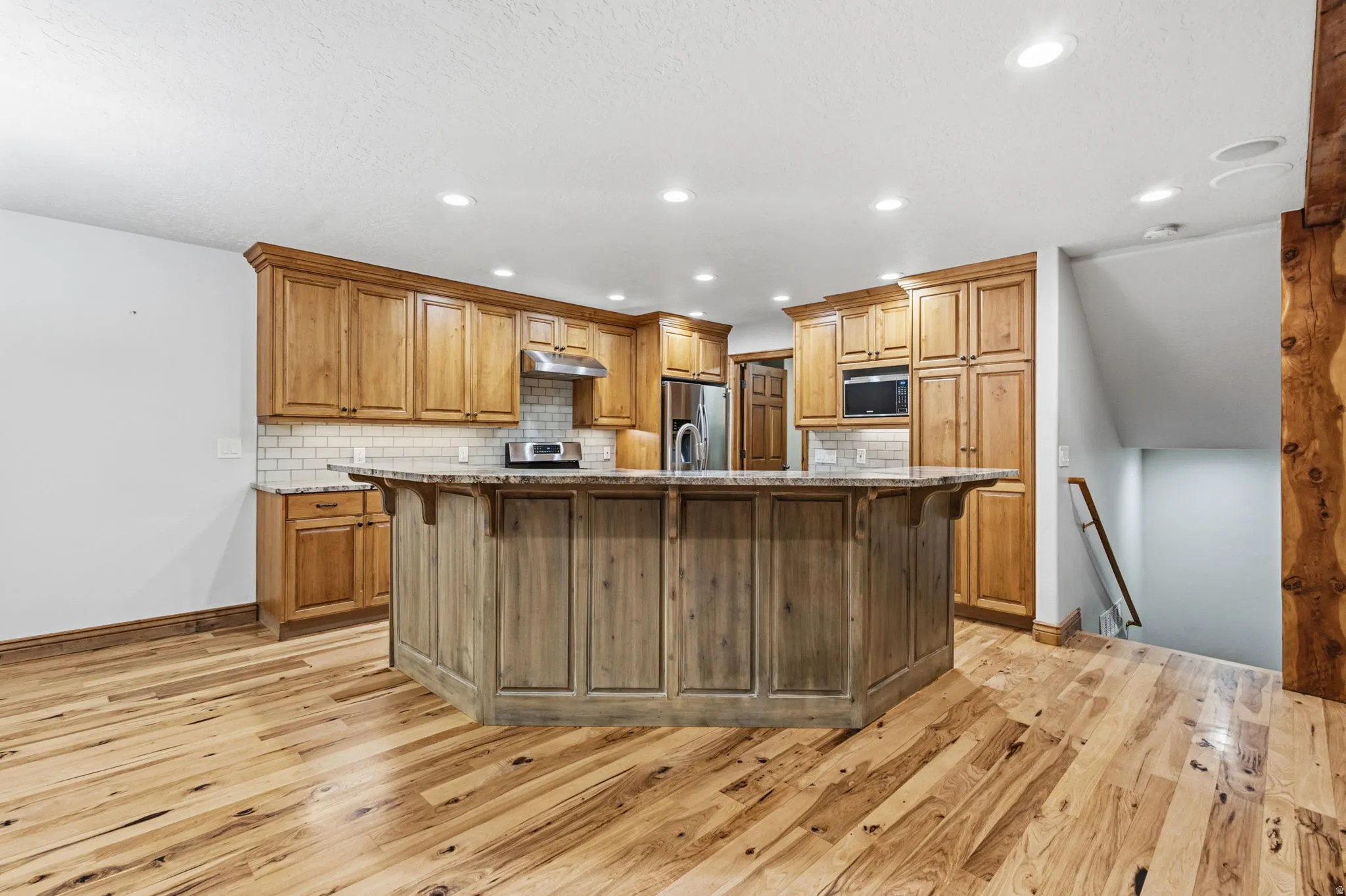Kitchen with a large island featuring panel detailing, wood-finish flooring, light wood cabinetry, a subway tile backsplash, and recessed lighting