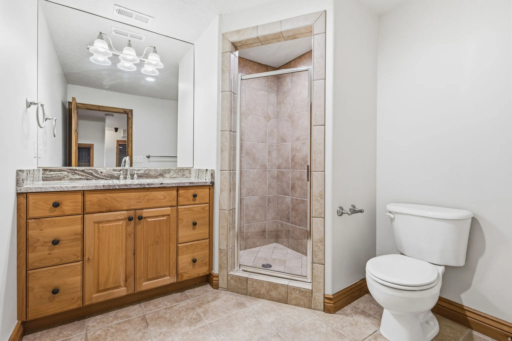 Bathroom featuring a wood vanity with a light-toned countertop, a frameless mirror, and a glass-enclosed shower with tiled walls