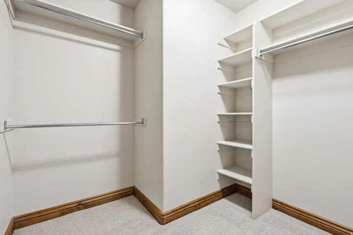 Carpeted walk-in closet featuring white walls, wood baseboards, multiple hanging rods, and built-in shelving