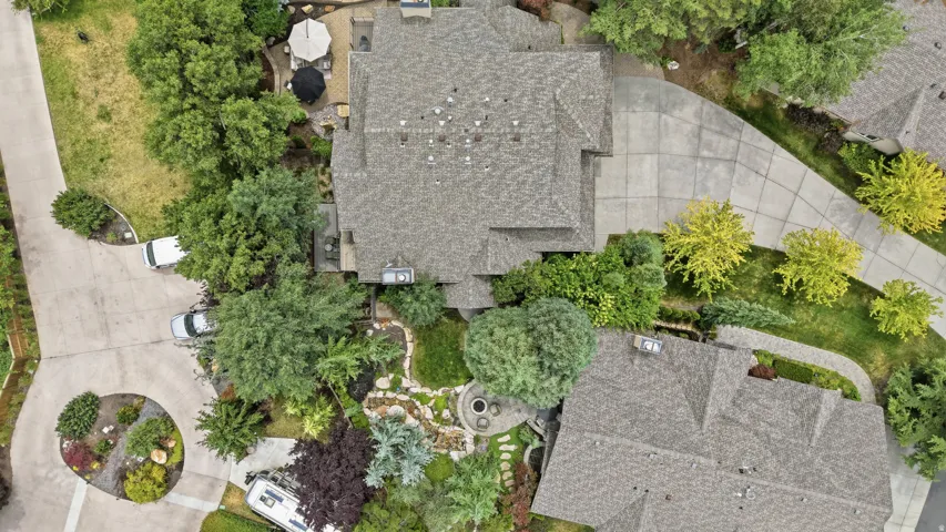 Property featuring a multi-gabled roofline, extensive paved driveways, a circular planting bed, a terraced patio, and mature landscaping