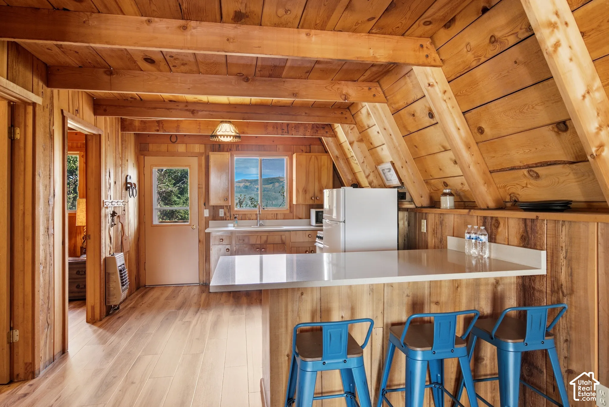 Kitchen & Breakfast Bar - Kitchen with a peninsula breakfast bar seating three, laminate countertops, and wood cabinetry beneath the sloped A-frame ceiling. A side door opens toward the deck.