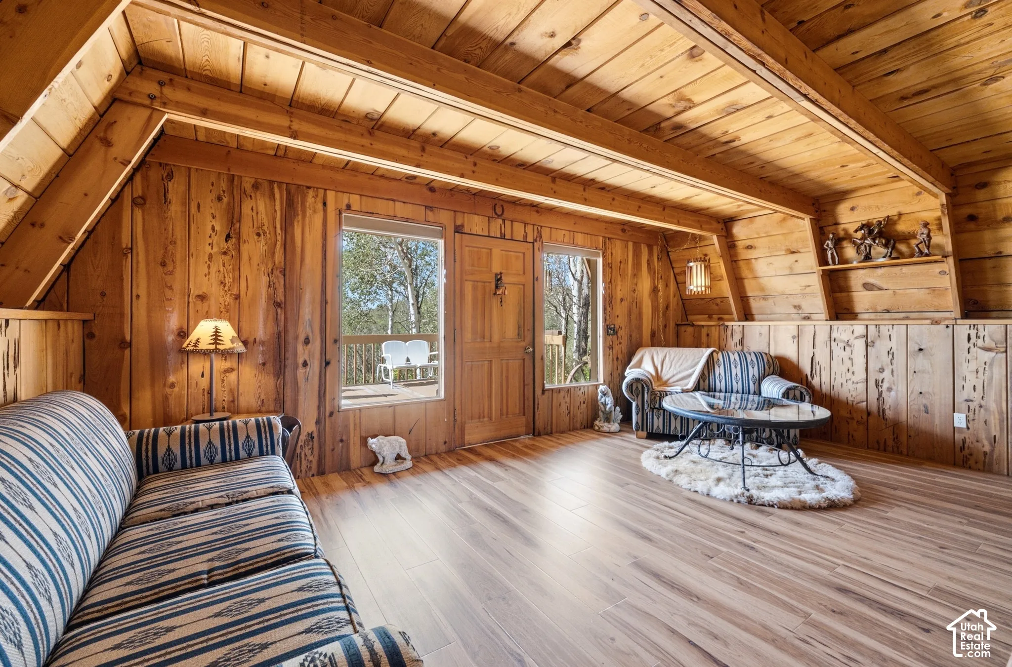 Main Living Area - Open living area with a door and windows to the front deck, sloped wood ceilings, and built-in shelving along the upper wall.