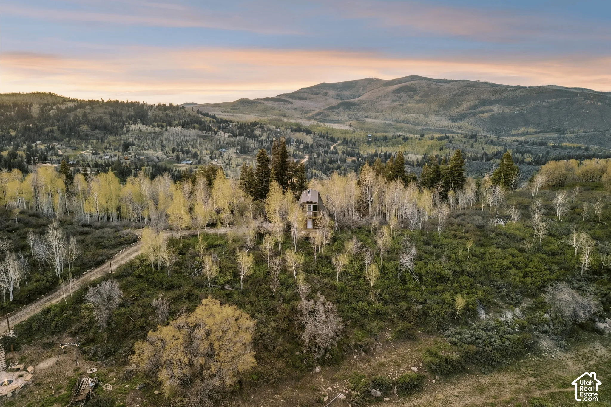 Aerial Context - The property in its broader setting, with access road, tree cover, and rolling terrain in all directions.