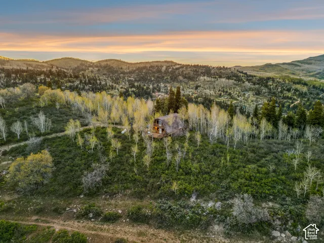 Aerial Exterior - A-frame cabin set among mature aspens and evergreens, with a standing-seam metal roof, upper balcony, and expansive wraparound deck overlooking the surrounding ridgeline.