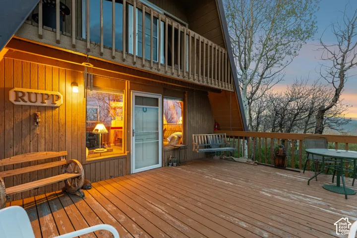 Front Deck at Dusk - Covered entry beneath the A-frame with a sliding glass door, porch swing, and bench seating, with interior lighting visible through oversized windows.