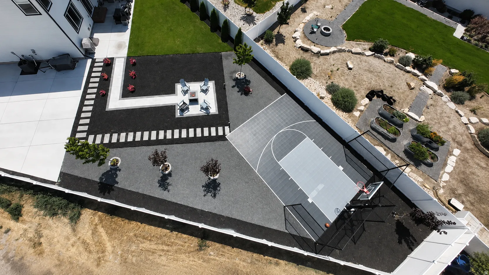 Expansive backyard featuring a half-court basketball court, a fire pit area with seating, diverse landscaping with gravel and turf, a concrete patio, and garden planters