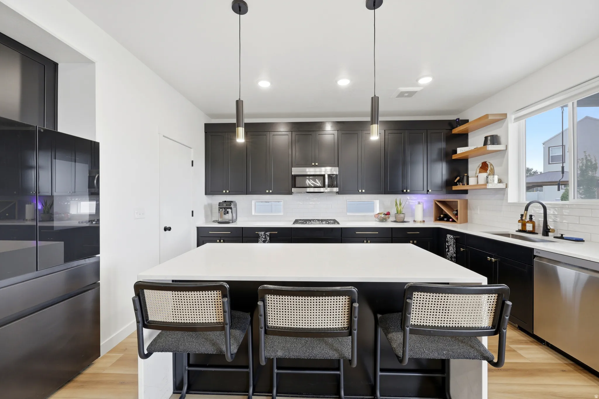 Modern kitchen featuring a large central island with seating, dark cabinetry, stainless steel appliances, and wood-finish flooring