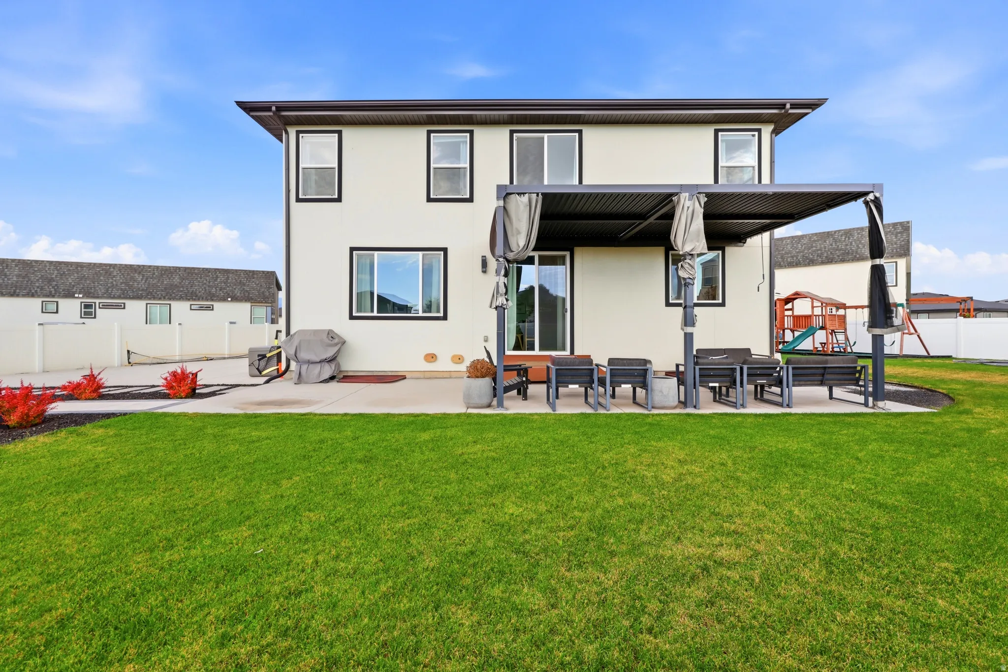 Expansive rear yard featuring a concrete patio, a pergola with retractable shades, and a large grassy area