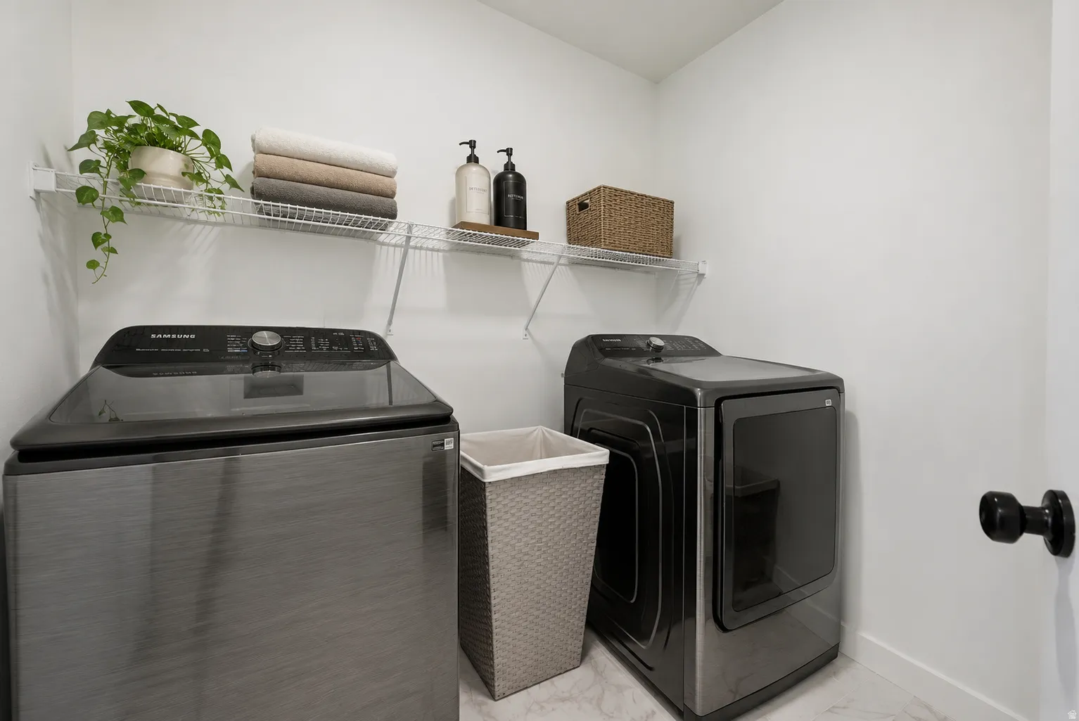 Dedicated laundry space featuring a washer and dryer, open wire shelving, and light-toned flooring