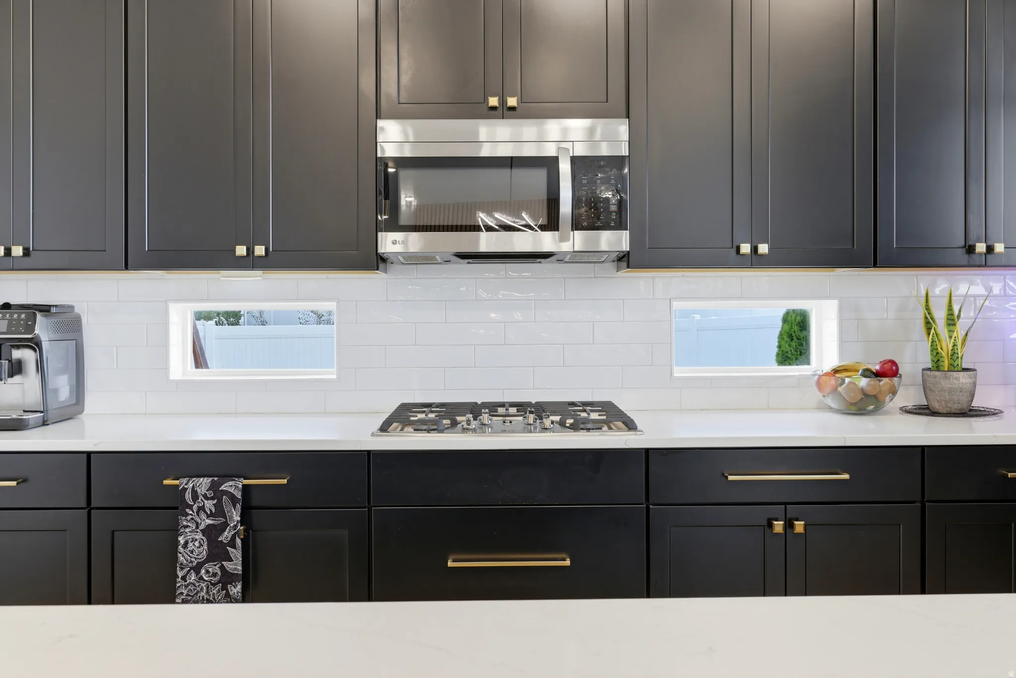 Contemporary kitchen featuring dark cabinetry with gold-toned hardware, white subway tile backsplash, and white countertops
