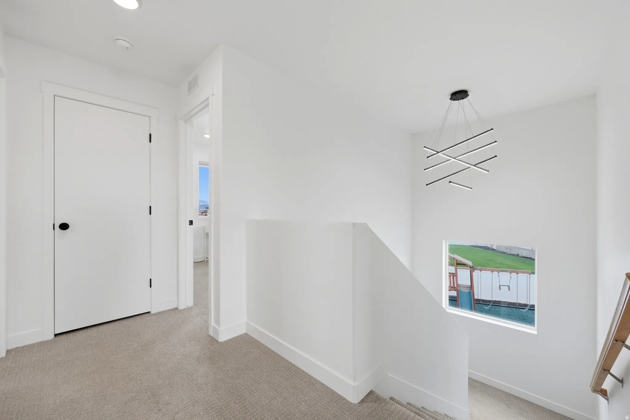 Hallway with light-toned carpet flooring, recessed ceiling lighting, and a modern chandelier