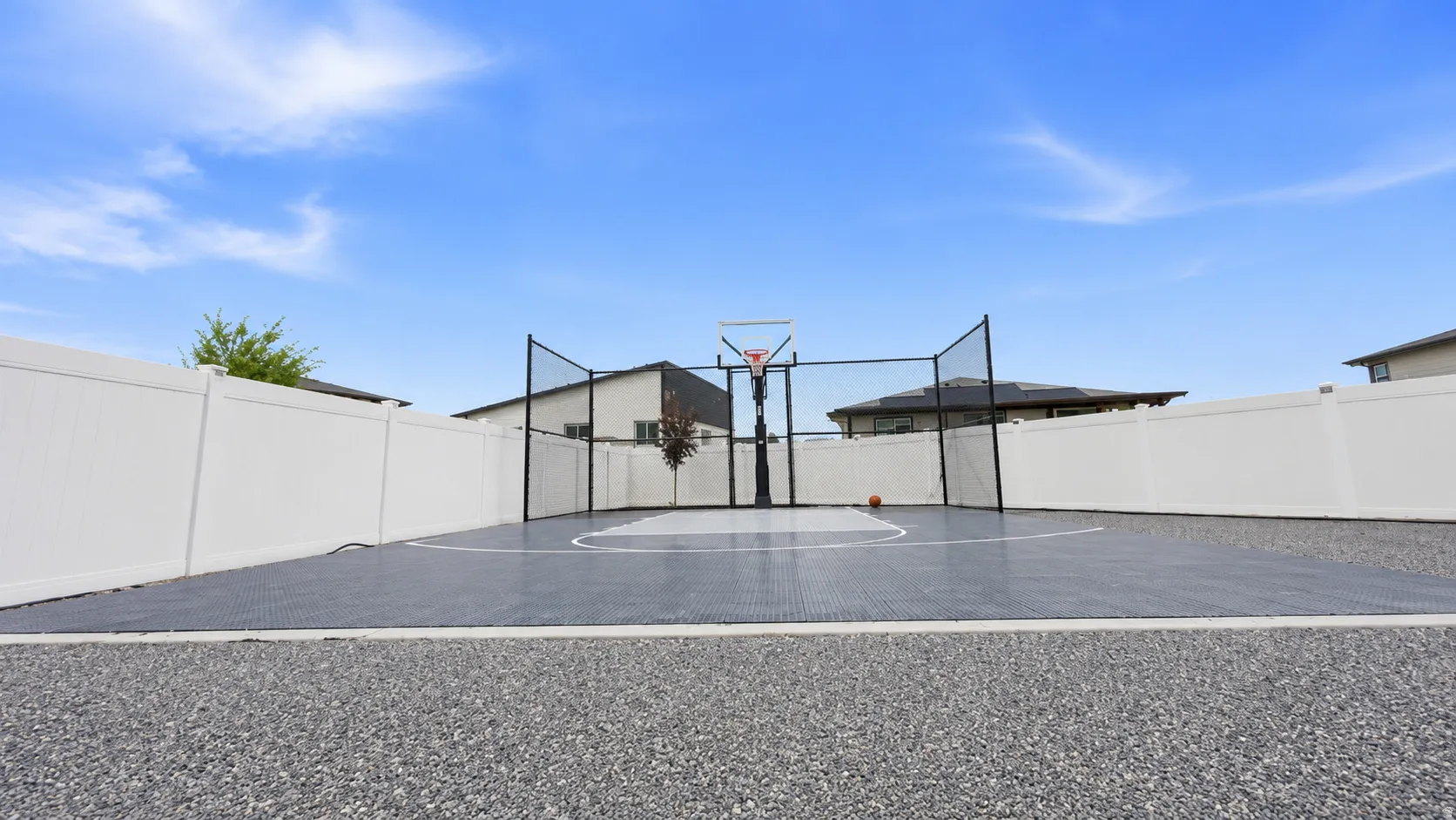 Outdoor sport court featuring a basketball hoop with a clear backboard, perimeter netting, and a low-maintenance, interlocking surface