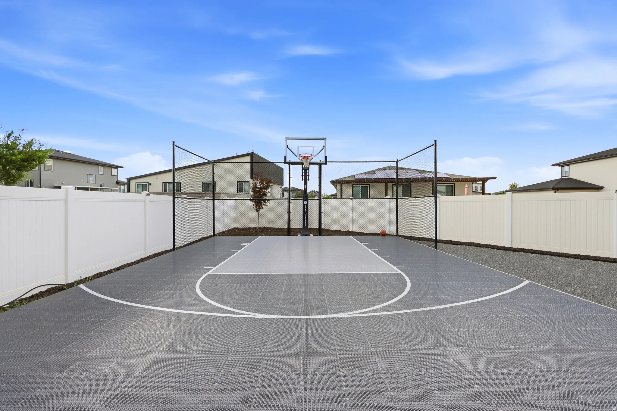 Dedicated sports court featuring a basketball hoop, perimeter fencing, and a durable gray and white surface