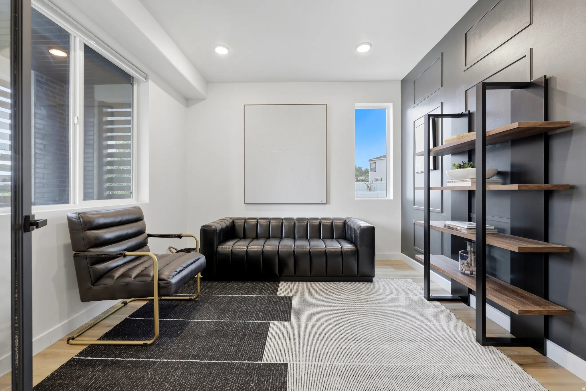 Recessed lighting illuminates a space featuring light wood-finish flooring, white walls, and a prominent dark accent wall with decorative panel molding