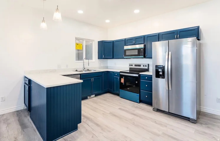 Modern kitchen featuring deep blue cabinetry with stainless steel appliances, including a built-in oven, cooktop, and refrigerator