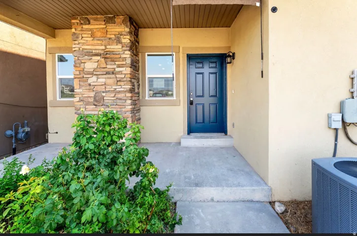 Modern entry courtyard featuring a stacked stone accent wall, blue painted entry door, concrete paver flooring, and mature climbing ivy landscaping