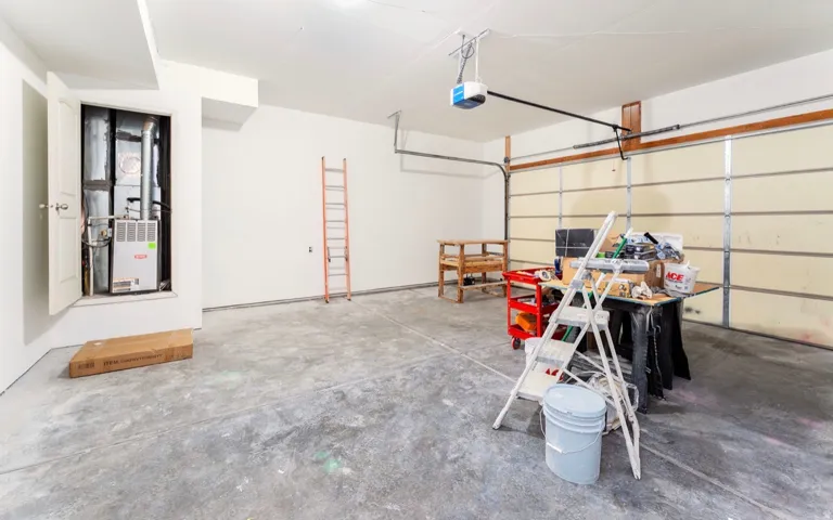 Spacious garage featuring polished concrete flooring, overhead garage door with integrated opener system, wall-mounted storage shelving, and direct interior access to the home