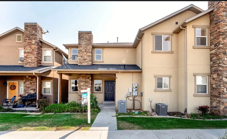 Contemporary townhome featuring a stucco and stone exterior with multiple chimneys, pitched rooflines, and a covered front porch