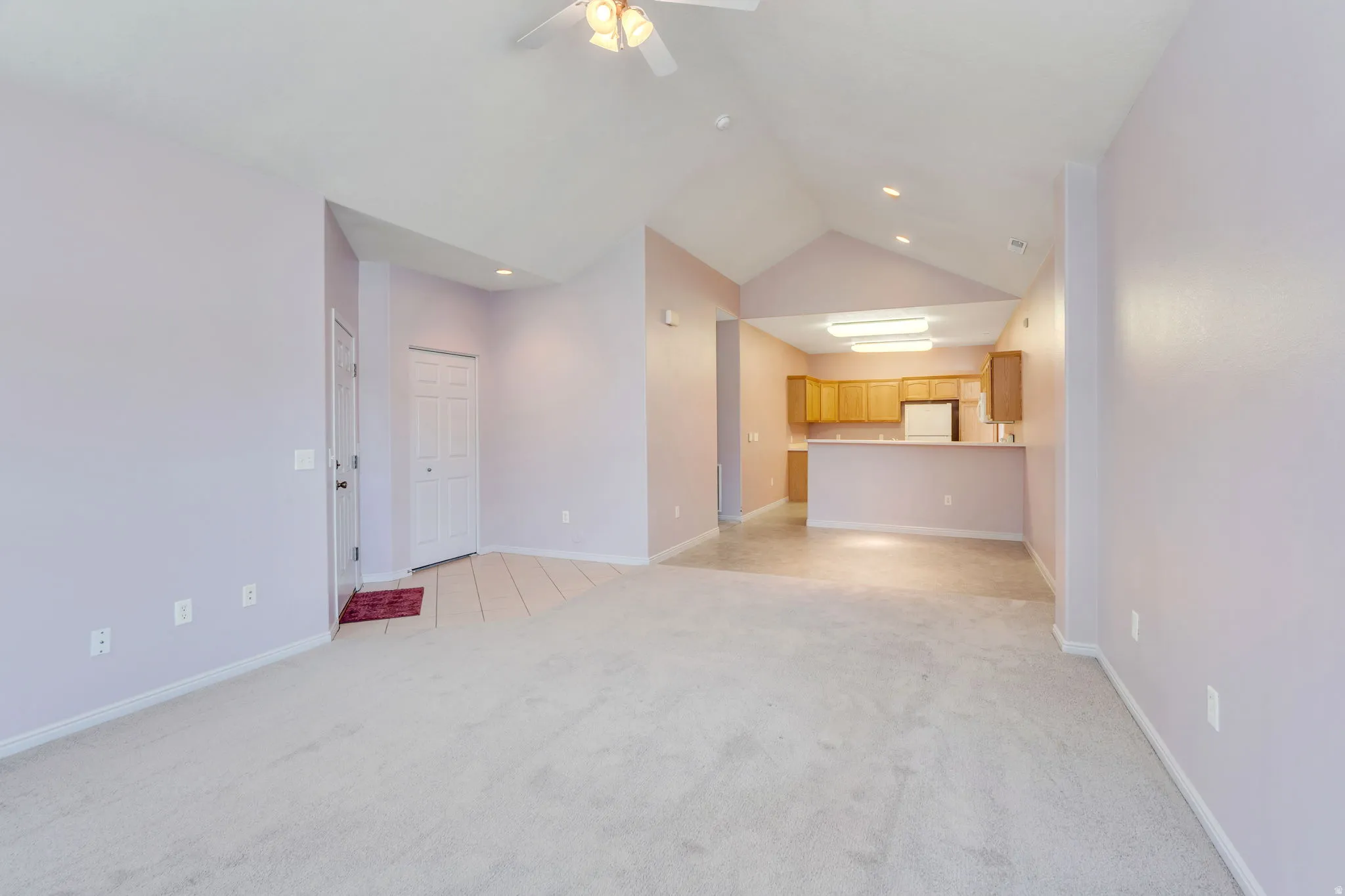 Open-concept room featuring vaulted ceilings, light-colored carpeting, and a ceiling fan