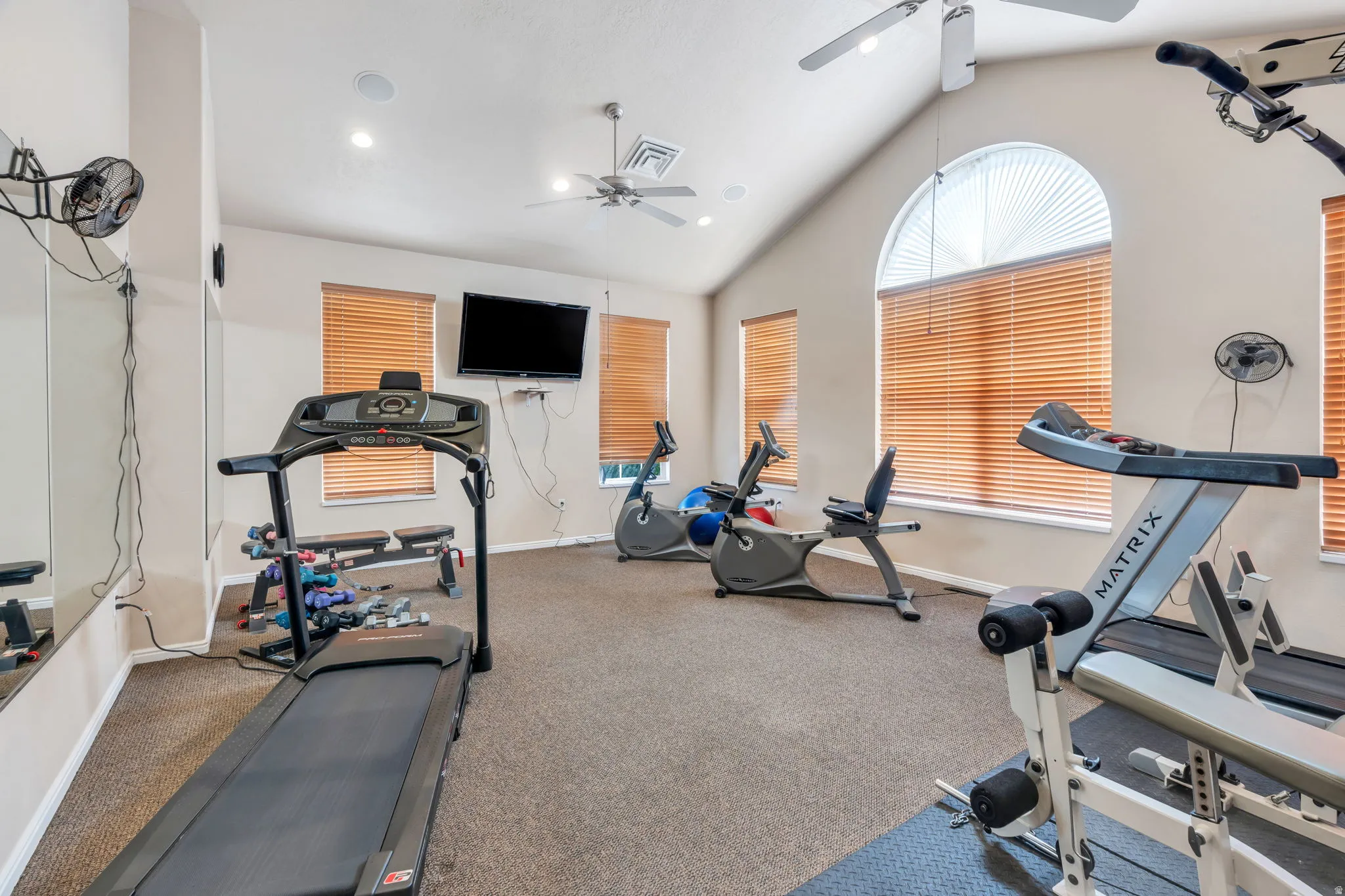 Dedicated fitness area featuring vaulted ceilings, recessed lighting, and multiple windows with horizontal blinds