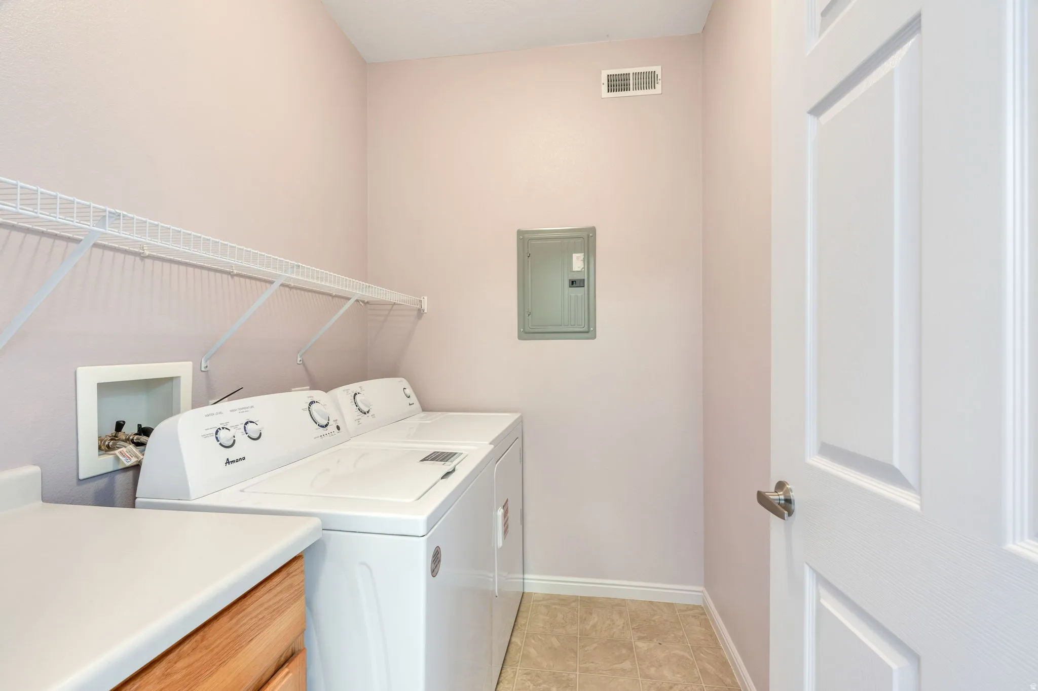 Dedicated laundry area featuring a full-size washer and dryer, wire shelving, a countertop, and wood-finish cabinetry