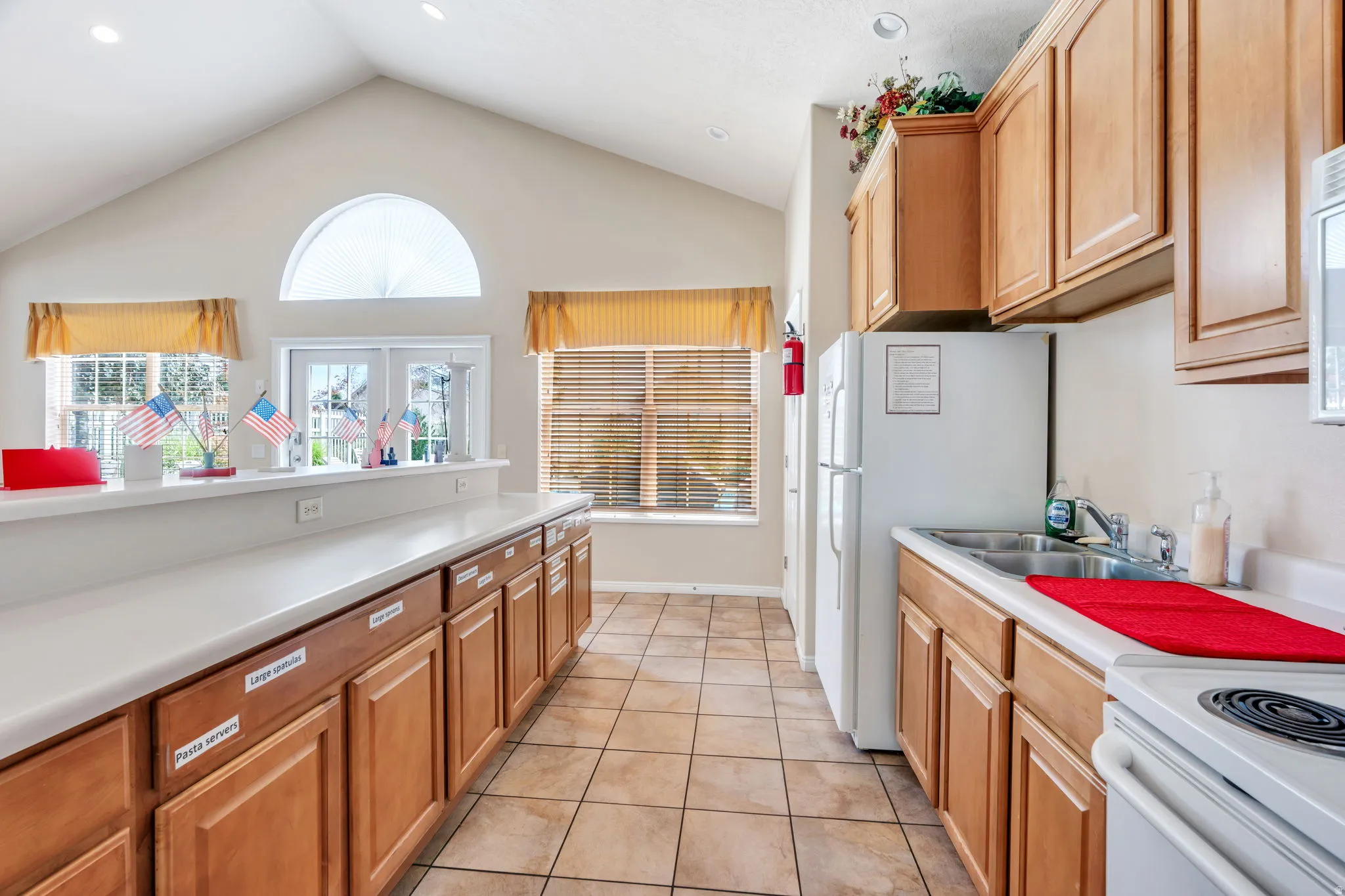 Vaulted ceiling kitchen featuring ample wood cabinetry, white countertops, tile flooring, and a double basin sink