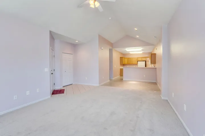 Open-concept room featuring vaulted ceilings, light-colored carpeting, and a ceiling fan