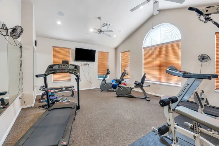 Dedicated fitness area featuring vaulted ceilings, recessed lighting, and multiple windows with horizontal blinds