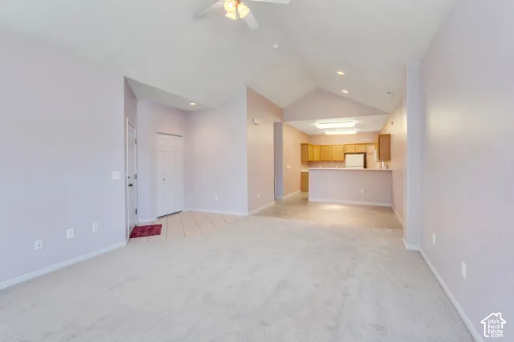 Open-concept room featuring vaulted ceilings, light-colored carpeting, and a ceiling fan