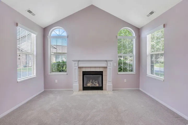 Vaulted ceiling room featuring a central fireplace with a decorative mantel, two arched windows, two rectangular windows, and light gray carpeting