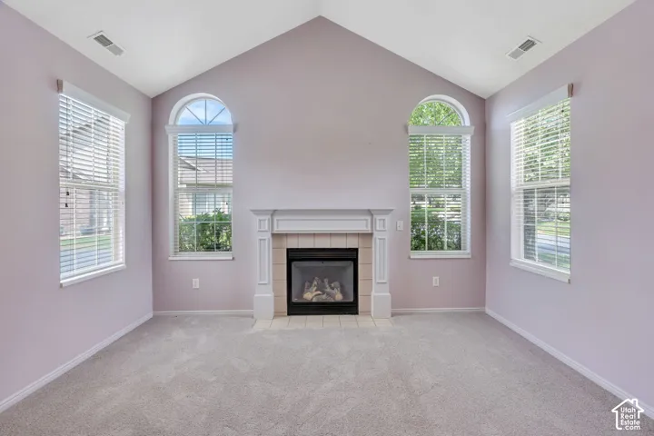 Vaulted ceiling room featuring a central fireplace with a decorative mantel, two arched windows, two rectangular windows, and light gray carpeting