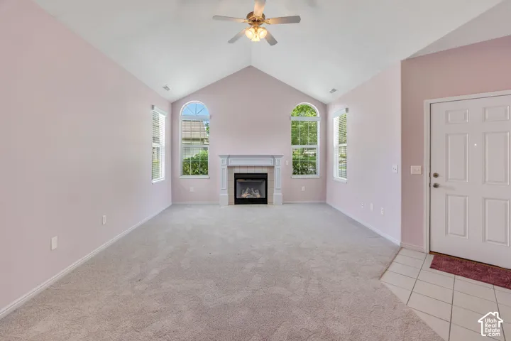 Vaulted ceiling living space featuring a fireplace with white mantel, two arched-top windows, ceiling fan, and light gray wall-to-wall carpeting