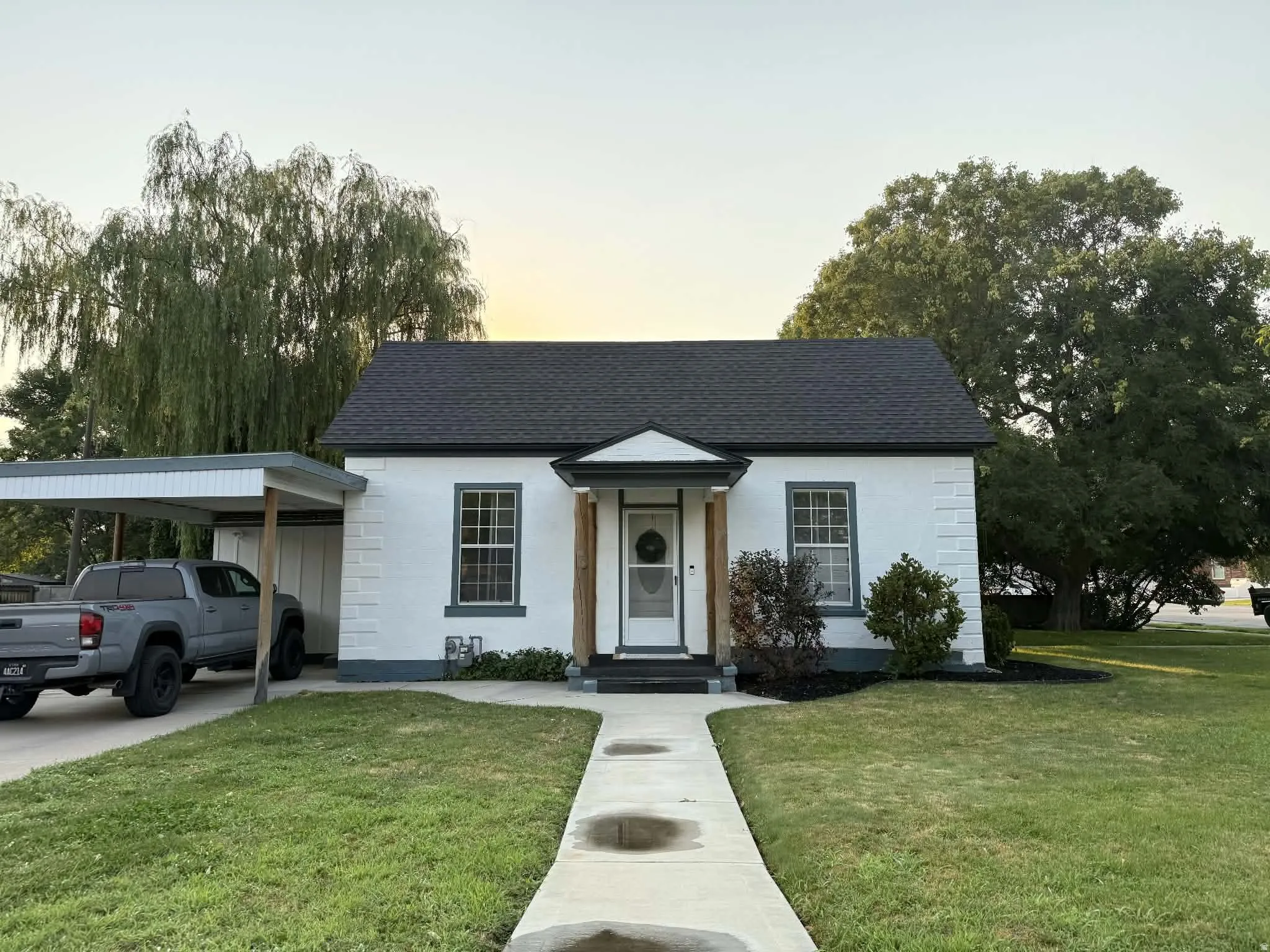 White facade with dark trim, featuring a dark shingle roof and a covered carport
