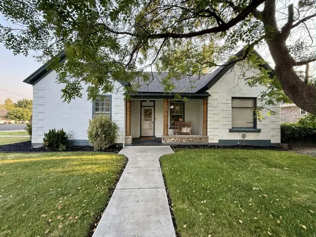 White exterior with stone accents, covered porch with wood-wrapped columns, dark gray roof, landscaped front yard, and concrete walkway