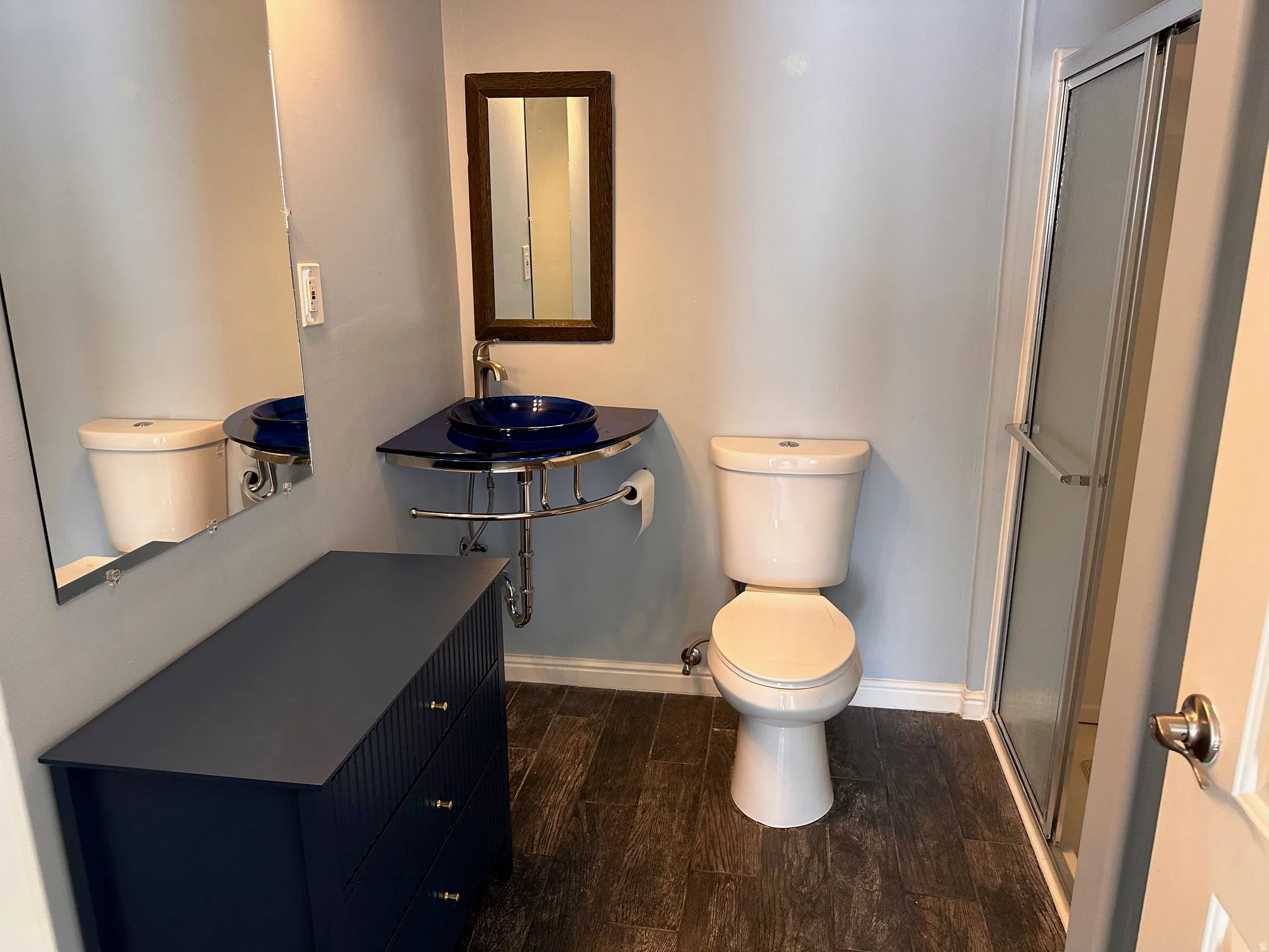 Contemporary bathroom featuring a corner vessel sink with a dark blue basin, a full-size toilet, and a stand-up shower with a frosted glass door