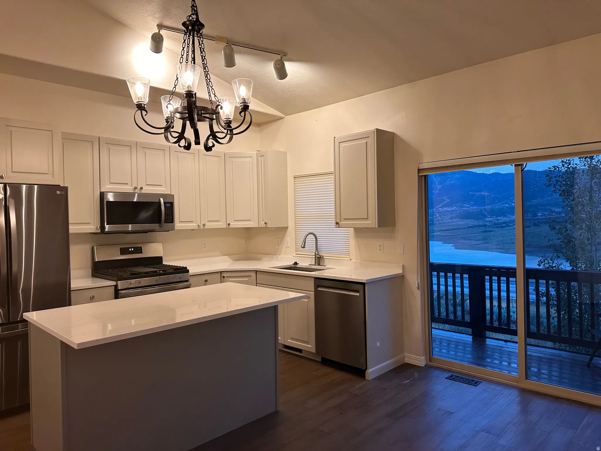 Contemporary kitchen featuring white cabinetry, stainless steel appliances, a center island with a light-toned countertop, and wood-finish flooring