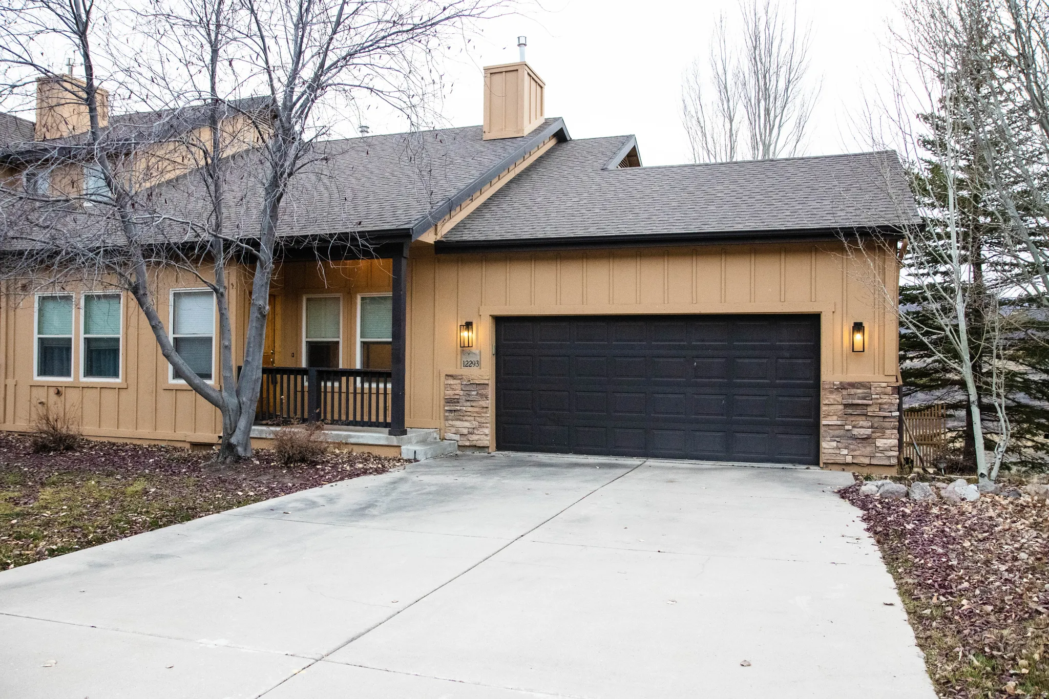 Exterior featuring a two-car garage with a dark panel door, a covered porch with a dark railing, and board and batten siding