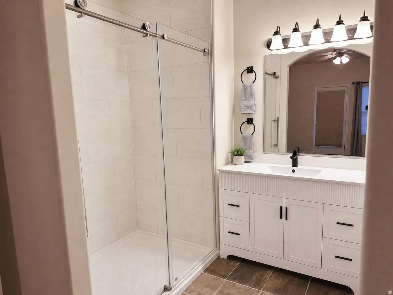 Modern bathroom featuring a glass-enclosed shower with tile surround, a white vanity with fluted details and dark hardware, a rectangular undermount sink, and a black single-handle faucet