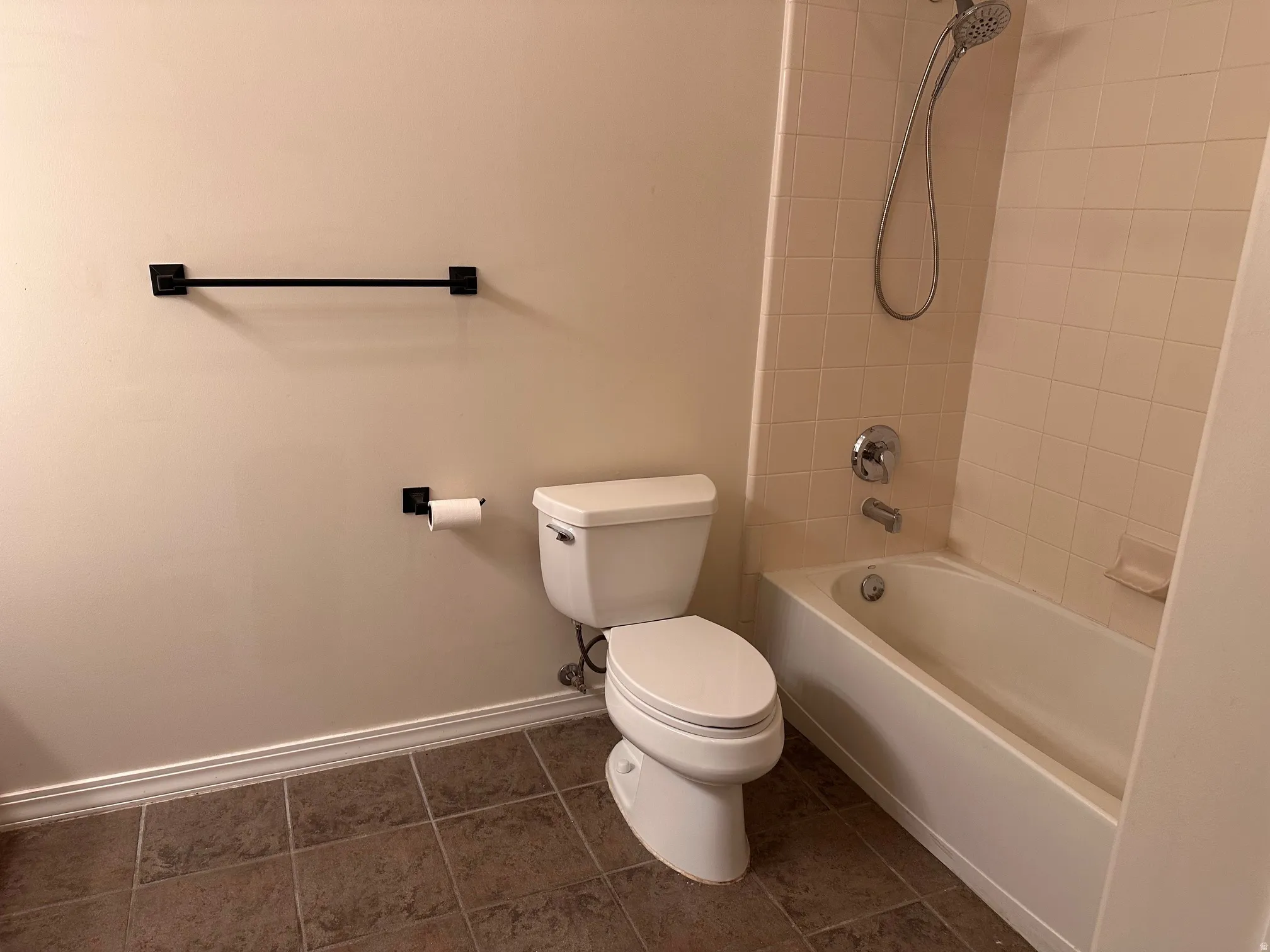 Bathroom featuring a white toilet, full-sized bathtub with shower, and beige wall tile